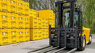 Ein gelber Gabelstapler mit Sechsfach-Palettengerät vor gelben Paketen mit Porenbeton