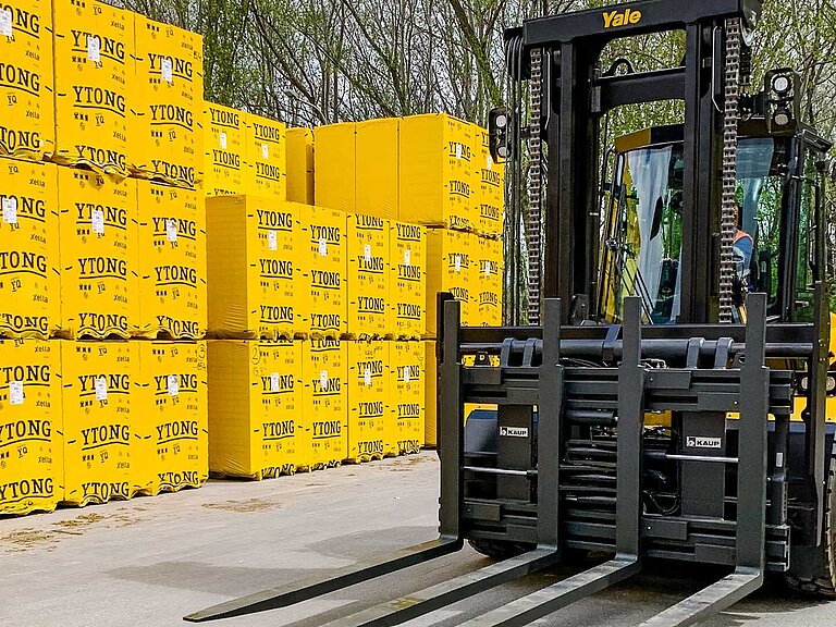 Ein gelber Gabelstapler mit Sechsfach-Palettengerät vor gelben Paketen mit Porenbeton