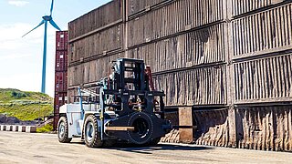 Eine große Baumaschine mit speziellem, drehbaren Anbaugerät manövriert über ein Bergbaugelände