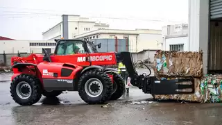 A red construction machine transports several stacked bales of waste paper with a mounted implement