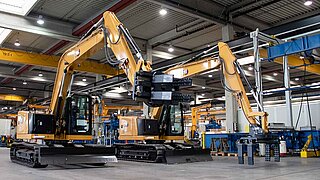 Two large yellow construction machines, equipped with bale clamps, stand side by side in a hall