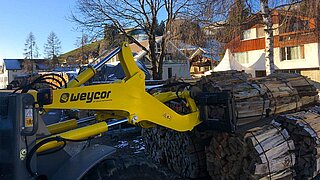 The long yellow arm of a construction machine picks up a large bundle of logs