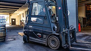 A black forklift truck with KAUP attachment on a company premises in front of wooden barrels