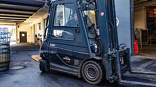 Ein schwarzer Gabelstapler mit KAUP-Anbaugerät auf einem Betriebsgelände vor Holzfässern