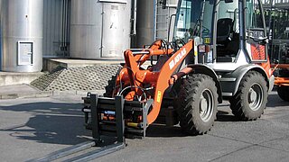 Une machine de construction, équipée d'une fourche de chariot élévateur, se trouve devant des silos