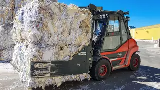 Eine rote Baumaschine transportiert einen gepressten Ballen Altpapier in einer Ballenklammer