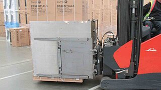 Seitenansicht eines roten Gabelstaplers mit Smart Load Control Anbaugerät und palettierter Ware