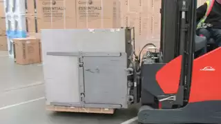 Seitenansicht eines roten Gabelstaplers mit Smart Load Control Anbaugerät und palettierter Ware