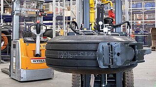 An aircraft tyre is lifted by a KAUP tyre clamp and transported through a warehouse