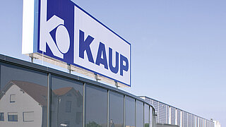 Großaufnahme des KAUP-Logos auf dem Dach einer Niederlassung vor blauem Himmel