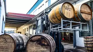 A forklift lifts and transports two barrels of spirits through a narrow aisle
