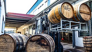 A forklift lifts and transports two barrels of spirits through a narrow aisle