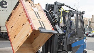 A blue forklift truck lifts several stacked wooden crates and rotates them through 45 degrees