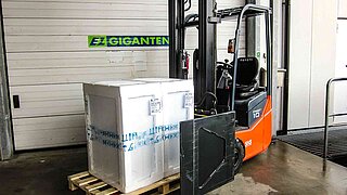 Forklift truck with goods packed in polystyrene on a wooden pallet in front of a roller shutter door