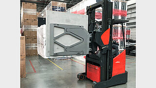 Ein roter Gabelstapler transportiert verpackte Warenpakete mit dem Smart Load Control Anbaugerät