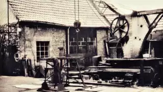 Historische Fotografie einer Schmiede mit diversen Apparaturen und einer gemauerten Scheune