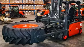 Ein roter Gabelstapler transportiert einen Reifen mithilfe einer Ballenklammer durch ein Lager