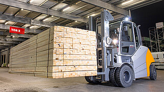 Un chariot élévateur transporte des lattes de bois empilées à l'aide d'un large accessoire