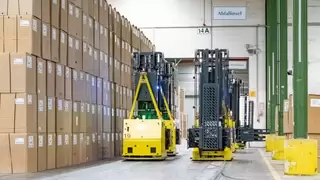Fahrerlose Transportsysteme bewegen sich entlang einer hohen Wand aus Kartons durch einen Gang