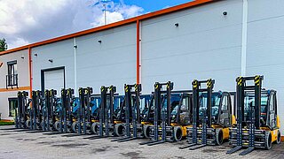 Several forklifts, equipped with identical clamping forks, are parked in a row