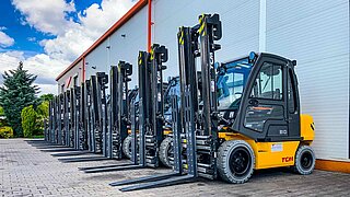 Several forklifts, equipped with identical clamping forks, are parked in a row