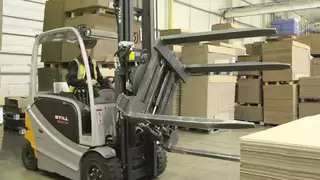 Ein silberner Gabelstapler mit drehbarem Anbaugerät lädt einen Stapel Kartons in einem Lager auf