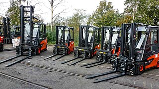 Five red forklifts with identical attachments are parked in a semicircle in an outdoor area