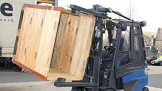 A blue forklift truck lifts several stacked wooden crates and rotates them through 45 degrees