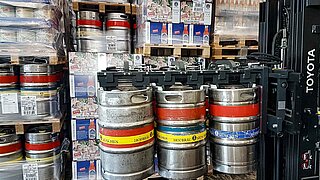 Silver beer kegs are lifted by a black attachment at the top by a forklift truck