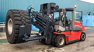 A red forklift truck equipped with a rotating clamp transports a large tyre