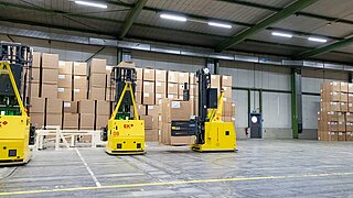 Three driverless transport systems transport stacked cardboard boxes through a warehouse