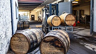 A forklift lifts and transports two barrels of spirits through a narrow aisle