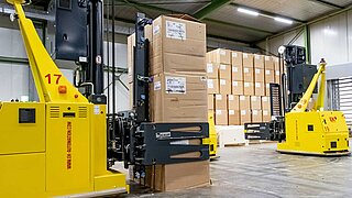 Two yellow, driverless forklift trucks transport piled-up boxes through a warehouse