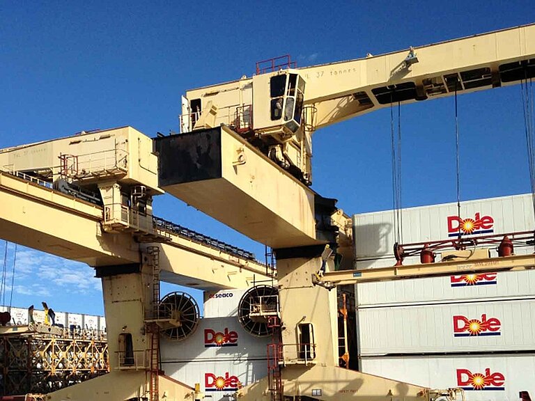 Two large yellow cranes with several stacked containers in the background