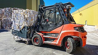 Eine rote Baumaschine transportiert mehrere gestapelte Altpapierballen mit einem Anbaugerät