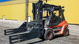 A red forklift truck with KAUP bale clamp stands in front of the yellow outer wall of a warehouse