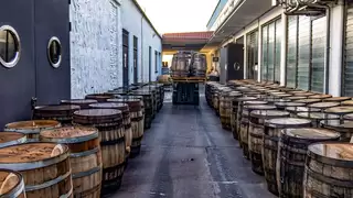A forklift truck moves through a narrow aisle lined with wooden barrels of spirits