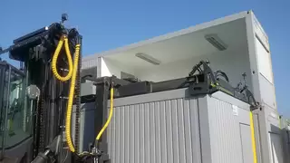 With the help of a wide attachment, a forklift picks up a container at the top