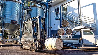 A forklift truck and a pick-up truck transport wooden barrels of spirits in front of a factory