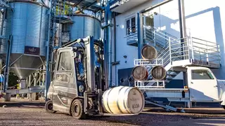 A forklift truck and a pick-up truck transport wooden barrels of spirits in front of a factory