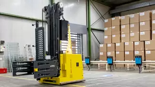 Ein fahrerloses Transportsystem steht vor aufgetürmten kartons in einer Lagerhalle