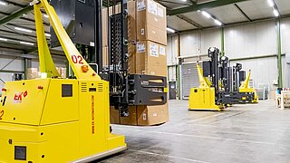 A driverless forklift truck transports a stack of boxes through a warehouse