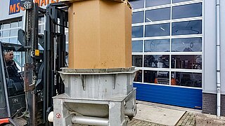 A red forklift truck takes a large cylindrical roll on a pallet onto the fork