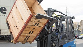 A blue forklift truck lifts several stacked wooden crates and rotates them through 45 degrees