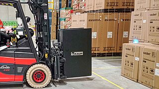 A red forklift truck with a black attachment drives towards several stored cartons