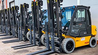 Several forklifts, equipped with identical clamping forks, are parked in a row