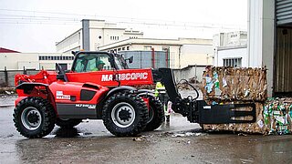 A red construction machine transports several stacked bales of waste paper with a mounted implement