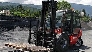 A red forklift truck transports two wooden pallets with four forks across a construction site