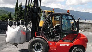 Eine Baumaschine transportiert mehrere volle, weiße Säcke, welche von den Staplergabeln hängen