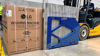 Ein Gabelstapler nimmt eine verpackte Waschmaschine mit dem Smart Load Control Anbaugerät auf